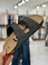 Sandalias de dos tiras negras con hebillas metálicas ajustables, plantilla anatómica y suela plana.