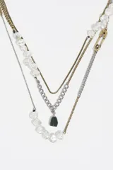 Collar multicapa de estilo vintage con cadenas combinadas en tonos dorados y plateados. Presenta aplicaciones de cuentas transparentes tipo perla, un dije de piedra oscura y un cierre decorativo tipo imperdible.