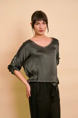 Blusa de satén color verde oscuro, de manga 3/4 con presilla y botón para arremangar, escote en V con ribete brillante y corte holgado.