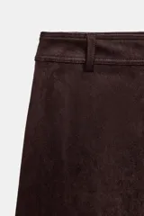 Falda midi de corte acampanado confeccionada en tejido con efecto ante color bordó. Presenta tiro medio, trabillas en la cintura y cierre frontal con cremallera y gancho metálico.