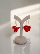 Aros colgantes dorados con diseño de flores rojas en relieve y detalle de perla sintética en el centro.