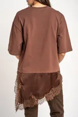 Remera oversize marrón con corte a la altura de la cadera, cuello redondo y mangas cortas holgadas. Incorpora un aplique inferior superpuesto de satén con detalles de encaje bordado en los bordes.