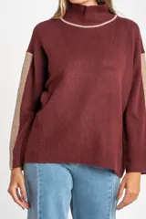 Polera de punto con calce oversize, cuello alto y mangas largas. Presenta un diseño en color negro con franjas laterales en las mangas y detalle en el cuello en tono bronce con acabado brillante.