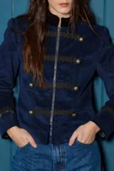 Blazer corto de estilo militar confeccionado en terciopelo azul marino, con cuello mao, cierre frontal con cremallera, detalles de galones bordados y botones metálicos decorativos.