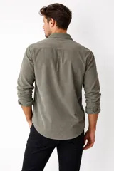 Camisa de pana color marrón, de manga larga, con cuello clásico abotonado y cierre frontal con botones.