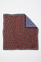 Pañuelo cuadrado estampado con diseño paisley en tonos rojo terracota y reverso azul, con bordes oscuros.