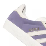 Championes Adidas modelo Gazelle ADV, confeccionados en gamuza color lavanda con las icónicas tres tiras y detalles en color crema. Presentan el nombre del modelo en letras doradas en el lateral y una suela de goma texturizada.