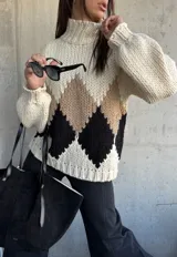 Sweater de punto grueso con cuello alto, diseño de rombos en tonos beige y negro sobre base color natural, de corte holgado y mangas largas con puños ajustados.