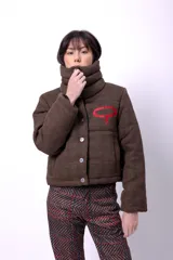 Campera corta con estampado abstracto en tonos marrones y beige, cuello alto, cierre frontal con botones a presión, bolsillos delanteros y bordado negro con las iniciales CP. Forro interior y relleno liviano de guata.