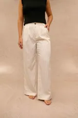 Pantalón de vestir color crudo con rayas diplomáticas negras, de tiro alto, corte sastrero y piernas anchas. Cuenta con bolsillos laterales y cierre frontal con botón carey.