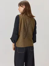 Chaleco de paño con diseño bicolor, frente en color negro y espalda en color marrón con textura de espiga. Presenta un maxi bordado de hoja en la parte posterior y detalles de tejido en los bordes.