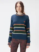 Sweater de punto cable con diseño a rayas horizontales en tonos marrón, amarillo y lila. Presenta cuello redondo acanalado, mangas largas con puños a juego y logo bordado en el pecho.