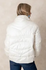 Campera puffer de acabado satinado en color beige, con cuello alto, cierre frontal y bolsillos laterales. Presenta un diseño moderno y sofisticado.