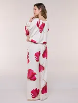 Conjunto de dos piezas de crep compuesto por una blusa holgada con escote en V y mangas largas abullonadas, y un pantalón palazzo tiro alto con pretina elástica. Presenta un estampado floral en tonos rosados sobre base blanca.