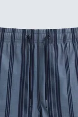 Bañador de hombre de largo medio, color azul claro con rayas verticales en azul oscuro. Posee cintura elástica ajustable con cordón, bolsillos laterales y un bolsillo trasero de plastrón.