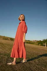 Vestido midi color ladrillo, de corte amplio, con cuello camisero, mangas 3/4 abullonadas y ruedo con volantes.