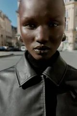 Cazadora corta negra de efecto piel, con cuello solapa, manga larga y cierre frontal con botones a presión ocultos. Incluye bolsillos delanteros de vivo con botón a presión y bajo con elástico en la espalda.