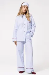 Pijama de dos piezas de algodón a rayas celestes y blancas, compuesto por una camisa de manga larga con botones y ribetes marrones, y un pantalón largo de corte recto con elástico en la cintura.