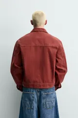 Cazadora cropped fit de Zara confeccionada en tejido de algodón con estructura canvas, de color bordó con efecto lavado. Cuenta con cuello solapa, manga larga con puños abotonados, bolsillos frontales de plastrón con solapa, parche bordado en el pecho y cierre frontal con cremallera.