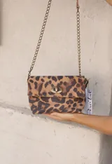 Cartera tipo bandolera con estampado animal print de leopardo. Posee una solapa frontal con cierre metálico giratorio en tono bronce y una correa de cadena metálica larga.