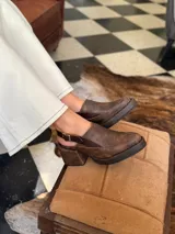 Zapato tipo zueco de cuero color chocolate con efecto desgastado, plataforma y taco cuadrado. Presenta una tira trasera ajustable con hebilla metálica.