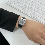 Reloj digital Casio de estilo vintage con caja plateada de 28mm y esfera gris. Cuenta con correa de cuero negro con textura tipo cocodrilo. Incluye funciones de cronómetro, alarma y calendario.