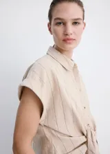 Camisa de lino y algodón color beige con estampado de raya diplomática, cuello camisero, manga corta y detalle de nudo en la cintura con cierre delantero de botones.