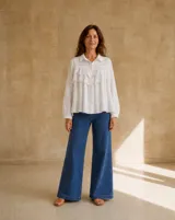 Camisa blanca de manga larga con cuello camisero, cierre frontal de botones y detalles de volados con bordado broderie en el frente.