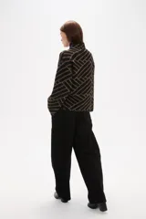 Sweater de tejido jacquard con diseño geométrico de líneas entrelazadas en tonos negro y marrón. Presenta cuello alto, mangas largas con terminación holgada y un corte recto.
