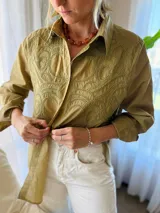 Camisa de manga larga color verde militar, con cuello clásico y cierre frontal de botones. Presenta un canesú bordado con diseño ornamental en la parte frontal superior.