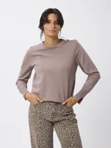 Buzo de punto fino color marrón topo, con cuello redondo y detalle de botones decorativos dorados sobre el hombro izquierdo. Presenta mangas largas con puños acanalados y una pequeña abertura lateral en los mismos.