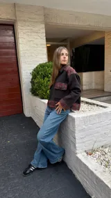 Campera de corte oversize confeccionada en lana merino, con diseño bicolor que combina paneles de color gris oscuro liso con detalles en tejido de punto con textura y estampado a cuadros en tonos rojizos y marrones. Presenta cierre frontal, cuello camisero, bolsillos frontales con solapa y puños con el mismo tejido estampado.