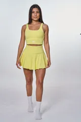 Conjunto deportivo compuesto por un top de escote redondo con logo estampado y una pollera short con diseño plisado, ambos en color amarillo.