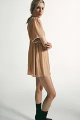 Vestido corto color tostado con escote cuadrado y mangas cortas. Presenta detalles de encaje en contraste en el escote y los bordes de las mangas. Cuenta con espalda descubierta y cierre posterior con cremallera oculta.