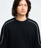 Remera de algodón color blanco, con cuello redondo, manga corta y detalle de raya negra contrastante que recorre la parte superior de los hombros y mangas. Diseño de corte holgado.