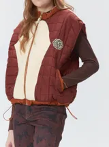 Chaleco de corte cuadrado con diseño bicolor en tonos terracota y crema. Presenta cierre frontal metalizado, parches de nylon en el pecho, interior forrado en corderito y cordón ajustable en el ruedo.