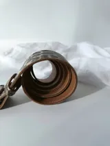 Cinto de cuero con estampado animal print y hebilla rectangular con diseño abstracto en blanco y negro.