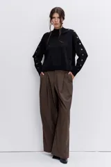 Sweater de punto negro con cuello alto y detalle de ojalillos metálicos a lo largo de las mangas. Presenta un corte holgado con puños y ruedo acanalados.