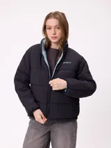 Campera puffer reversible de la marca Rusty, con diseño capitoneado. Presenta cuello alto, cierre frontal completo y logo bordado en el pecho. El interior es de un tono contrastante.