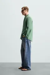 Camisa celeste a rayas verticales, de corte relaxed fit, confeccionada en lino y algodón. Tiene cuello abotonado, manga larga con puños abotonados, bolsillo de parche en el pecho y cierre frontal con botones.