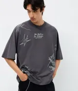 Remera de corte oversized color gris oscuro, con cuello redondo y manga corta. Presenta una estampa gráfica en la espalda que incluye un ángel, estrellas y el lettering 'No Mercy' junto a la frase 'Las calles no perdonan'.