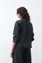 Camisa de jean color azul claro con tachas metálicas en el canesú y a lo largo de las costuras frontales. Tiene mangas largas con puños abullonados y cierre frontal con botones.