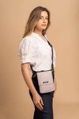 Phonebag pequeña color mostaza, confeccionada en cuero sintético, con solapa frontal y correa ajustable con logo de la marca.