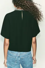 Remera negra de corte recto y holgado, con cuello redondo decorado con apliques de brillos y mangas cortas. Presenta una abertura en la espalda con cierre de botón oculto.