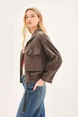 Campera de corte amplio, color marrón, con cierre frontal, bolsillos frontales con solapa y cintura ajustable. Incluye un pin decorativo en la solapa.