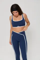 Conjunto deportivo compuesto por un top de escote cuadrado y calzas largas de tiro alto con diseño cruzado en la cintura. Ambas piezas son de color azul con detalles de ribetes blancos en los bordes y laterales. El top cuenta con el logo de la marca estampado en el frente.