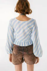 Top corto de lino italiano a rayas verticales beige y blanco, con escote en V, jareta ajustable con lazo en el centro delantero y volado en el ruedo. Mangas largas estilo globo con puños elásticos.