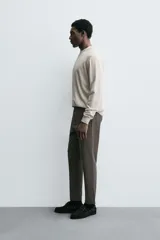 Pantalón de corte slim fit y color negro, confeccionado en tejido elástico. Cuenta con cintura elástica, trabillas, bolsillos frontales y cierre con cremallera y botón.