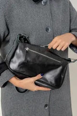 Cartera de hombro color bordó, confeccionada en cuero con acabado brillante. Presenta detalles de remaches metálicos plateados en los laterales y la base, y una correa ajustable con hebilla. Incluye una placa metálica con el logo de la marca en la parte frontal.