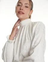 Blusa de gasa labrada color blanco, con cuello alto en punto smock, mangas largas con terminación fruncida y diseño elegante.